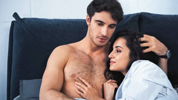 Shirtless boyfriend talking and hugging smiling girlfriend in white shirt at home — Stock Photo