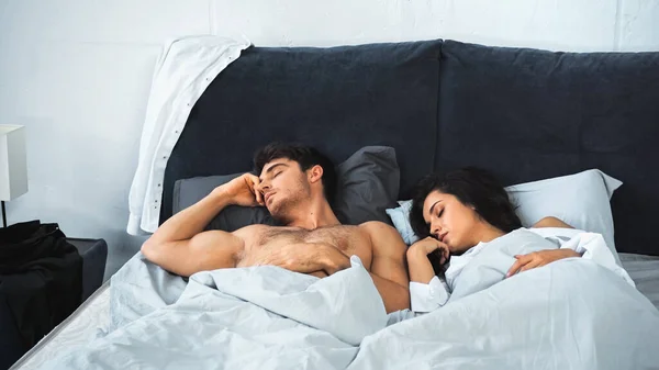 Shirtless man and brunette woman with closed eyes sleeping in bed — стоковое фото