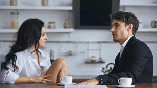 Бизнесмен разговаривает с улыбчивой девушкой в белой рубашке возле чашек кофе — стоковое фото