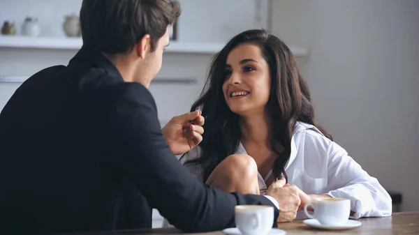 Businessman talking with happy girlfriend in white shirt and holding hands near cups of coffee — Photo de stock