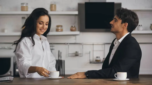 Happy businessman looking at sensual girlfriend in white shirt reaching cup of coffee - foto de stock