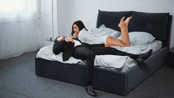 Homem de negócios deitado na cama e conversando com a namorada morena em camisa branca — Fotografia de Stock