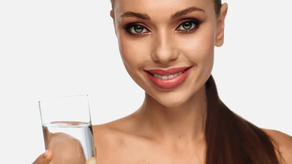 Portrait of happy young woman with makeup on face holding glass of water isolated on white — Stock Photo