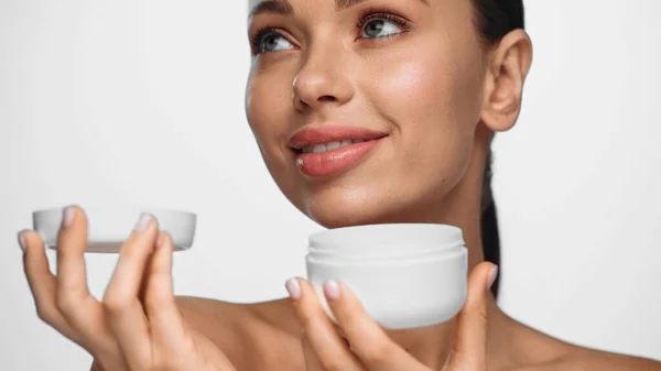 Portrait of happy young woman holding container with cream isolated on white — стоковое фото