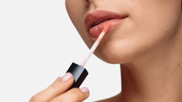 Cropped view of young woman applying lip gloss isolated on white - foto de stock