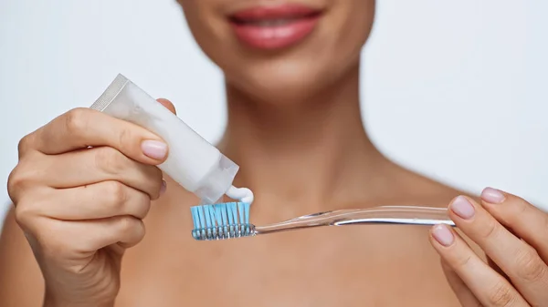 Обрезанный вид веселой молодой женщины, сжимающей зубную пасту на зубной щетке, изолированной на белом — стоковое фото