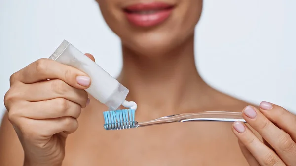 Cropped view of cheerful young woman squeezing toothpaste on toothbrush isolated on white — Stock Photo