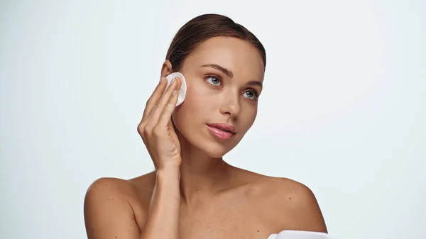 Jovem morena aplicando toner no rosto com almofada de algodão isolado no branco — Fotografia de Stock