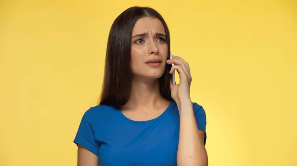 Young brunette woman in blue t-shirt talking on smartphone isolated on yellow — Photo de stock