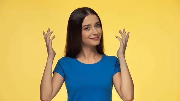 Young and smiling woman in blue t-shirt gesturing isolated on yellow — Stock Photo