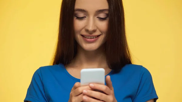 Young brunette woman smiling while chatting on mobile phone isolated on yellow - foto de stock