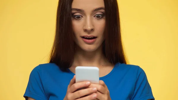 Молода і здивована жінка спілкується на мобільному телефоні ізольовано на жовтому — стокове фото