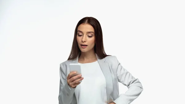 Erstaunt Geschäftsfrau im grauen Blazer schaut auf Smartphone isoliert auf weiß — Stockfoto