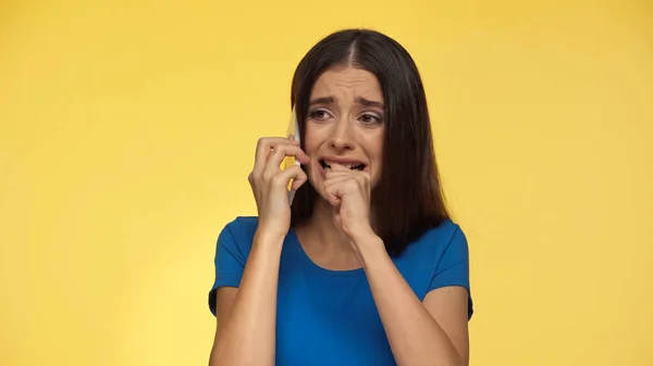 Young brunette woman in blue t-shirt crying while talking on smartphone isolated on yellow — Stock Photo