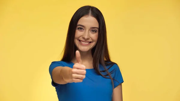 Young and happy woman in blue t-shirt showing thumb up isolated on yellow — Stock Photo