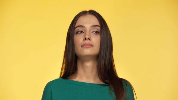 Skeptical and brunette young woman in green blouse isolated on yellow — Stock Photo