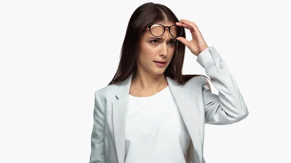 Confused businesswoman in grey blazer adjusting eyeglasses isolated on white — стоковое фото