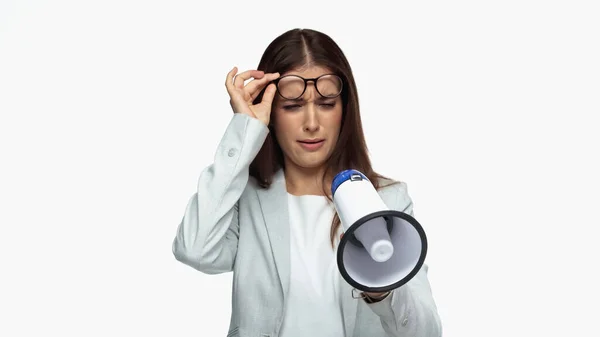 Young businesswoman in grey blazer adjusting eyeglasses and looking at loudspeaker isolated on white — Stock Photo