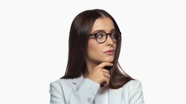 Curious businesswoman in grey blazer and eyeglasses looking away isolated on white — стоковое фото