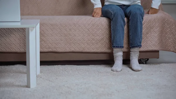 Cropped view of woman in jeans sitting on couch near coffee table with laptop — стоковое фото