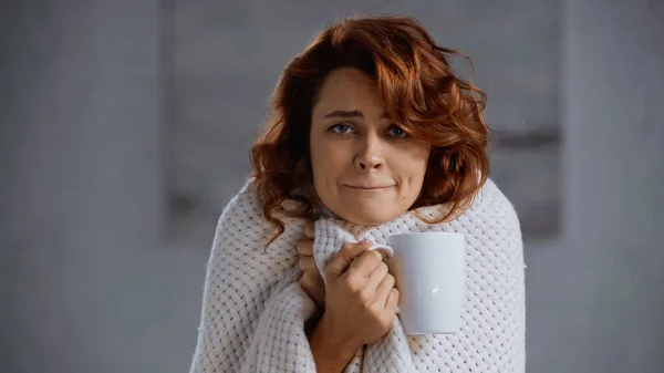 Redhead and sick woman covered in blanket holding cup with hot beverage — Stock Photo