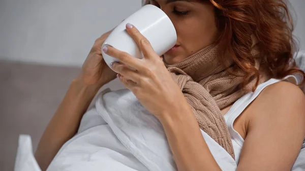 Donna malata in sciarpa in possesso di tazza e bere bevanda a casa — Foto stock