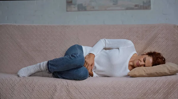 Junge Frau liegt auf Sofa und leidet unter Krämpfen und Bauchschmerzen — Stockfoto