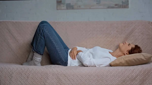 Mujer joven acostada en el sofá y sufriendo de dolor abdominal — Stock Photo