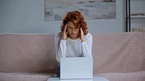 Tired redhead woman suffering from headache while sitting near laptop — Stock Photo