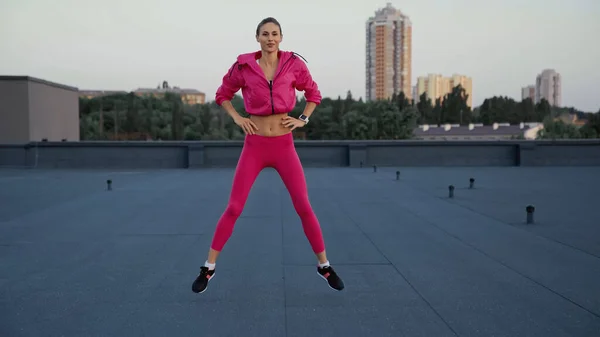 Sportswoman in pink sportswear jumping while training on roof - foto de stock