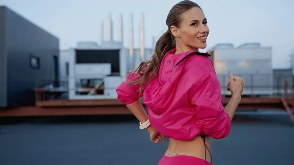 Cheerful sportswoman running while training on roof in evening — Fotografia de Stock