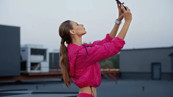 Side view of sportswoman pouting lips while taking selfie on smartphone on roof — Stock Photo