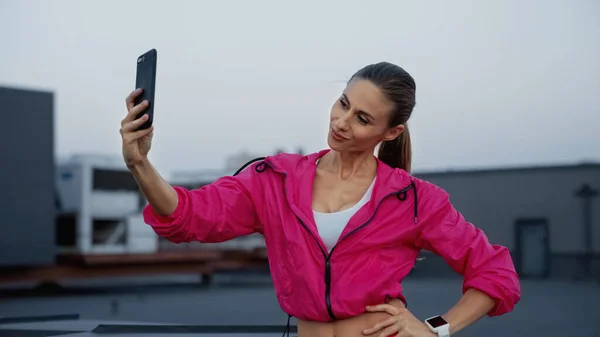 Smiling sportswoman taking selfie on smartphone on roof in evening — Photo de stock