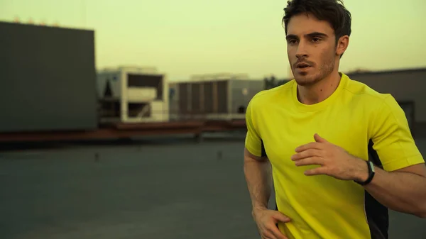 Young brunette sportsman running on roof of building in evening — Stock Photo