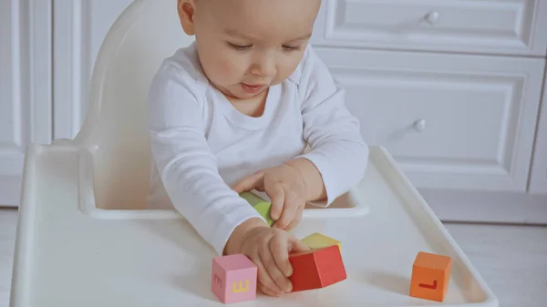 Focused baby girl sitting in feeding chair and playing with wooden cubes — Foto stock