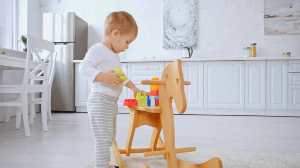 Toddler child playing with building blocks on rocking horse in spacious apartment — Stock Photo