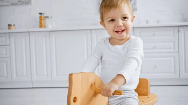 Happy toddler boy laughing and riding wooden rocking horse at home — Foto stock
