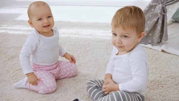 Cheerful toddler sister and brother sitting together on carpet at home — Foto stock