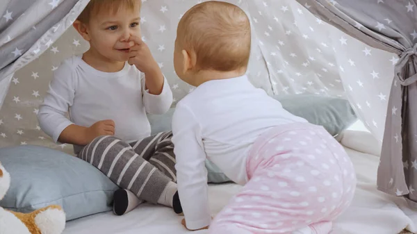 Little sister looking at toddler brother while sitting together in teepee at home — Foto stock