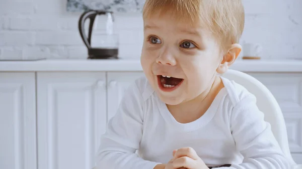 Excited toddler boy with opened mouth sitting in feeding chair at home — Stock Photo