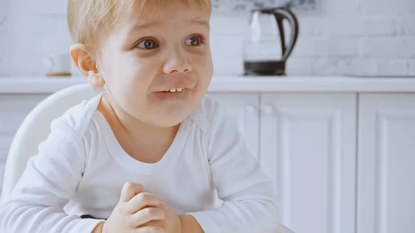 Cheerful toddler boy sitting in feeding chair while looking away at home — Stock Photo