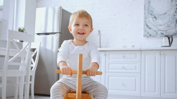 Joyful toddler kid smiling and riding wooden rocking horse at home — Photo de stock