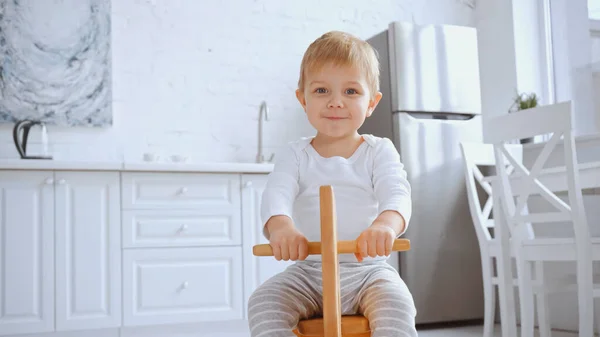 Positive toddler child smiling and riding wooden rocking horse at home — Foto stock