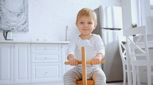 Positive toddler child smiling and riding wooden rocking horse at home — Stock Photo