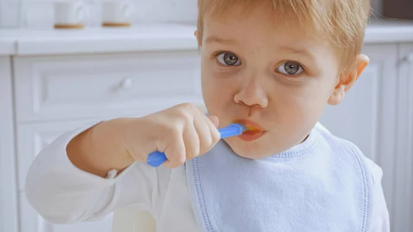 Toddler boy with grey eyes holding spoon and eating carrot puree — Stock Photo