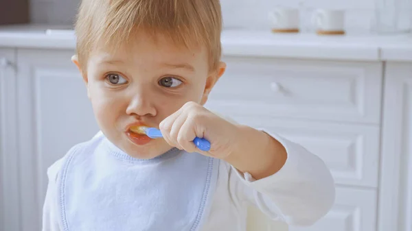 Toddler child with grey eyes holding spoon and eating carrot puree — Stock Photo