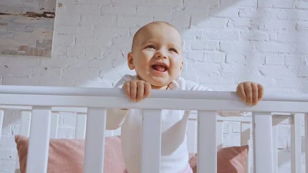 Low angle view of excited baby girl standing in white baby crib at home — Stock Photo