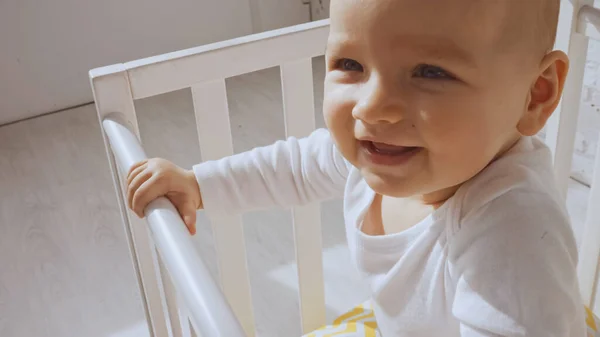 Close up of cheerful baby girl standing in white baby crib at home — Stock Photo