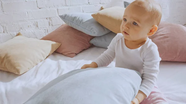 Adorable baby girl holding soft pillow and sitting on bed — Stock Photo