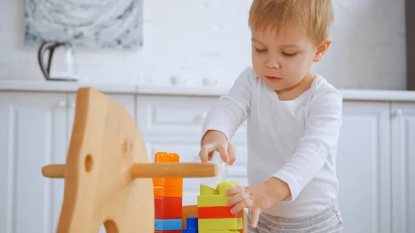 Toddler boy playing with building blocks on wooden rocking horse in apartment — Stock Photo